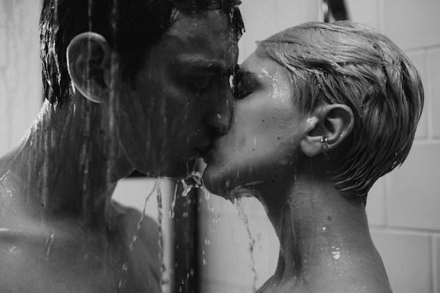 Black-and-white photograph of two people kissing under a shower, water streaming down as they embrace in an intimate, emotionally charged moment.