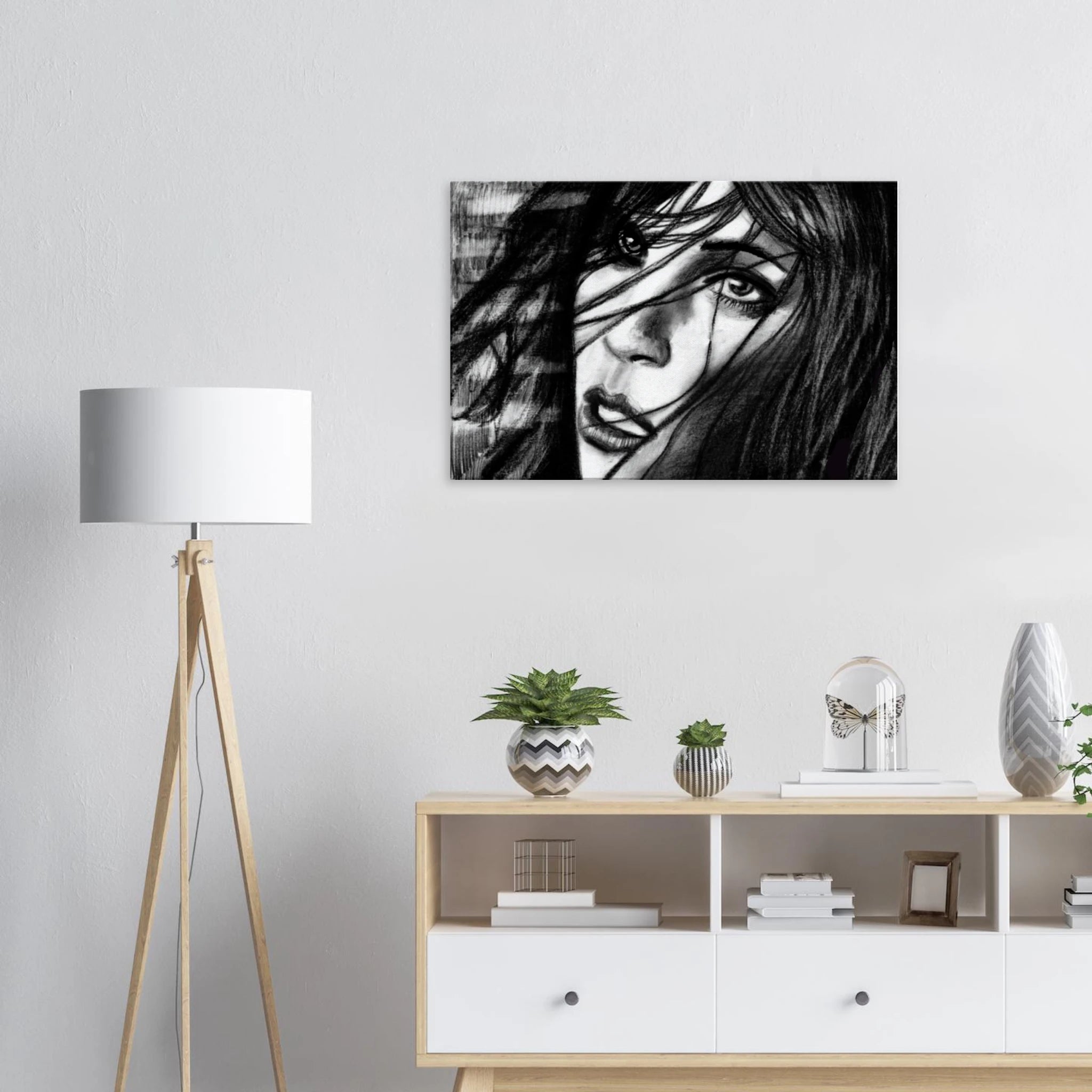 Black and white portrait art of a woman with flowing hair on a white wall above a wooden shelf with plants and decor